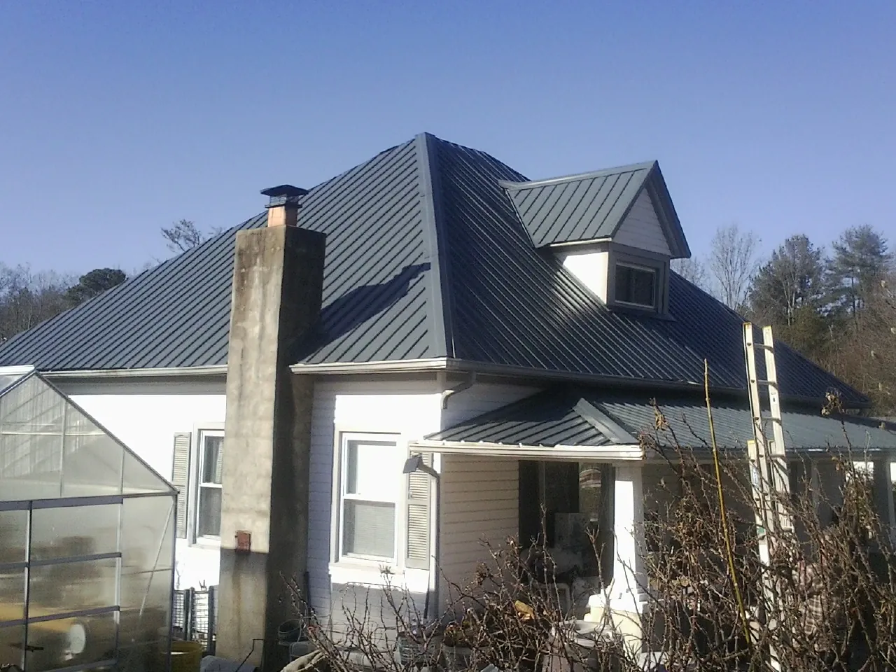 Dark blue standing seam metal roof on a white farmhouse with dormer — Slate & Tile Roof Repair by Roofing Brothers in Atalissa