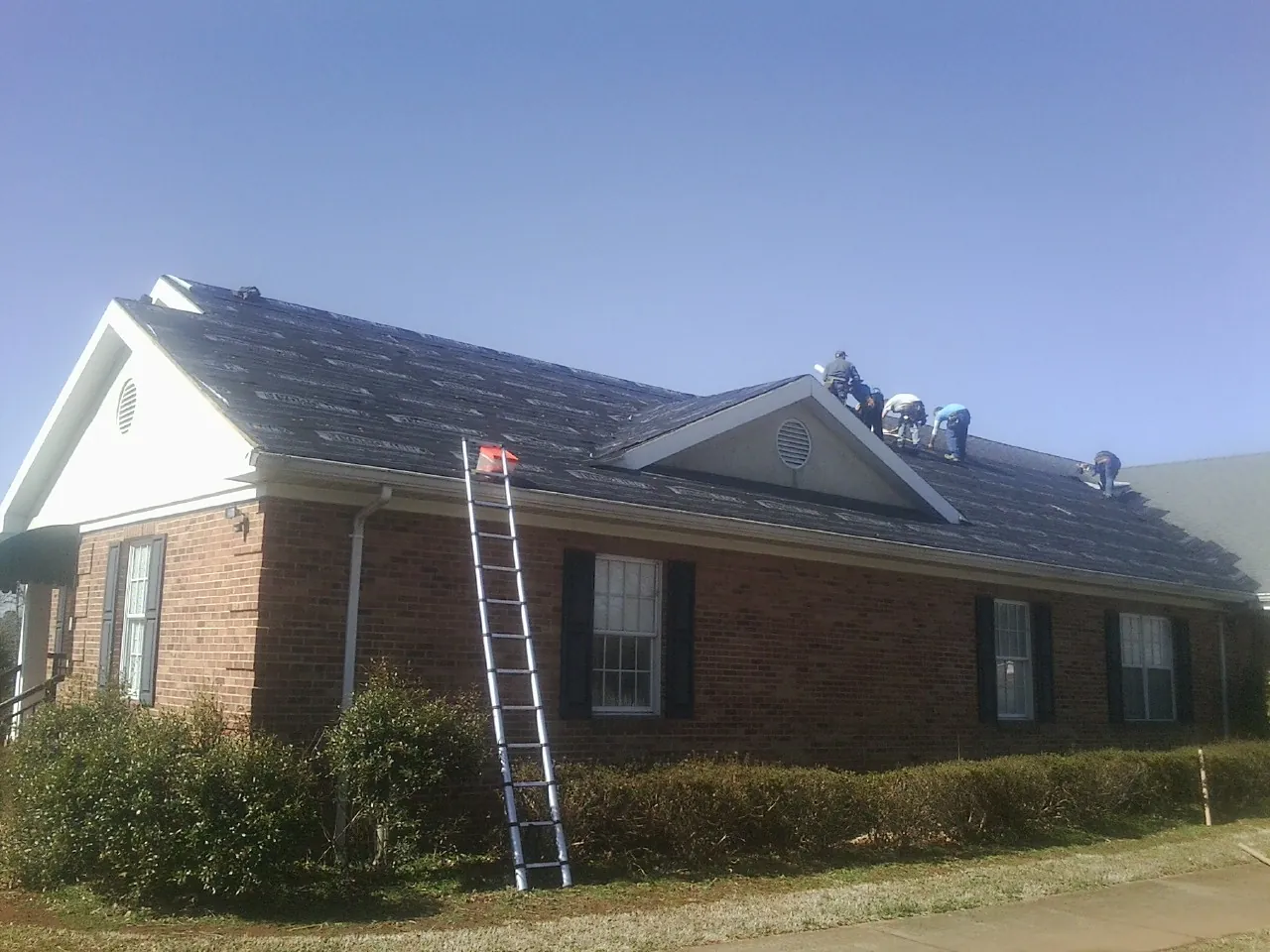 Crew tearing shingles off a brick ranch roof with a ladder set — Emergency Roof Repair work by our crew in Atalissa