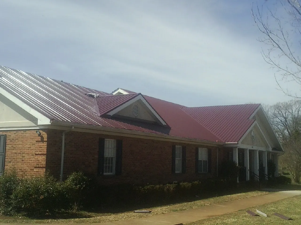 Red metal roof with gabled entries on a long brick building, from a Hail Damage Roof Repair job in Atalissa