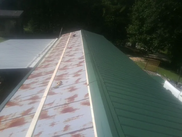 Old rusted panels beside newly installed green metal roofing — Wind Damage Roof Repair by Roofing Brothers in Atalissa