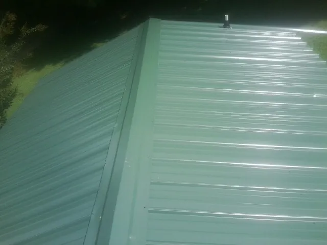 New green metal panels meeting at the ridge of a roof — Flat Roof Repair work by our crew in Atalissa