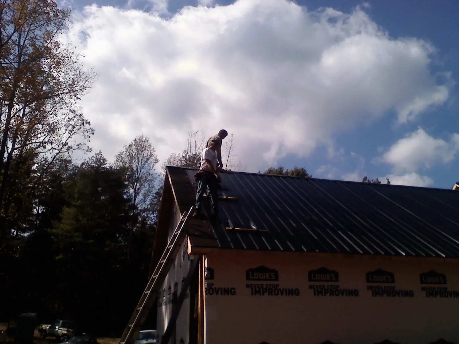 Roofer fastening dark metal panels high against a cloudy sky, from a Roof Inspection job in Atalissa